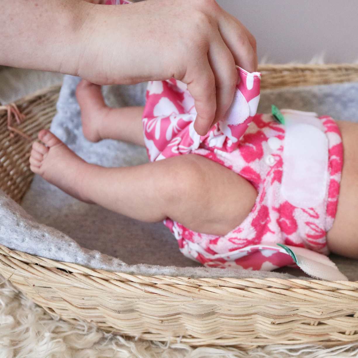 Parent putting on Reusable Nappy pink and white pattern in changing basket with blanket
