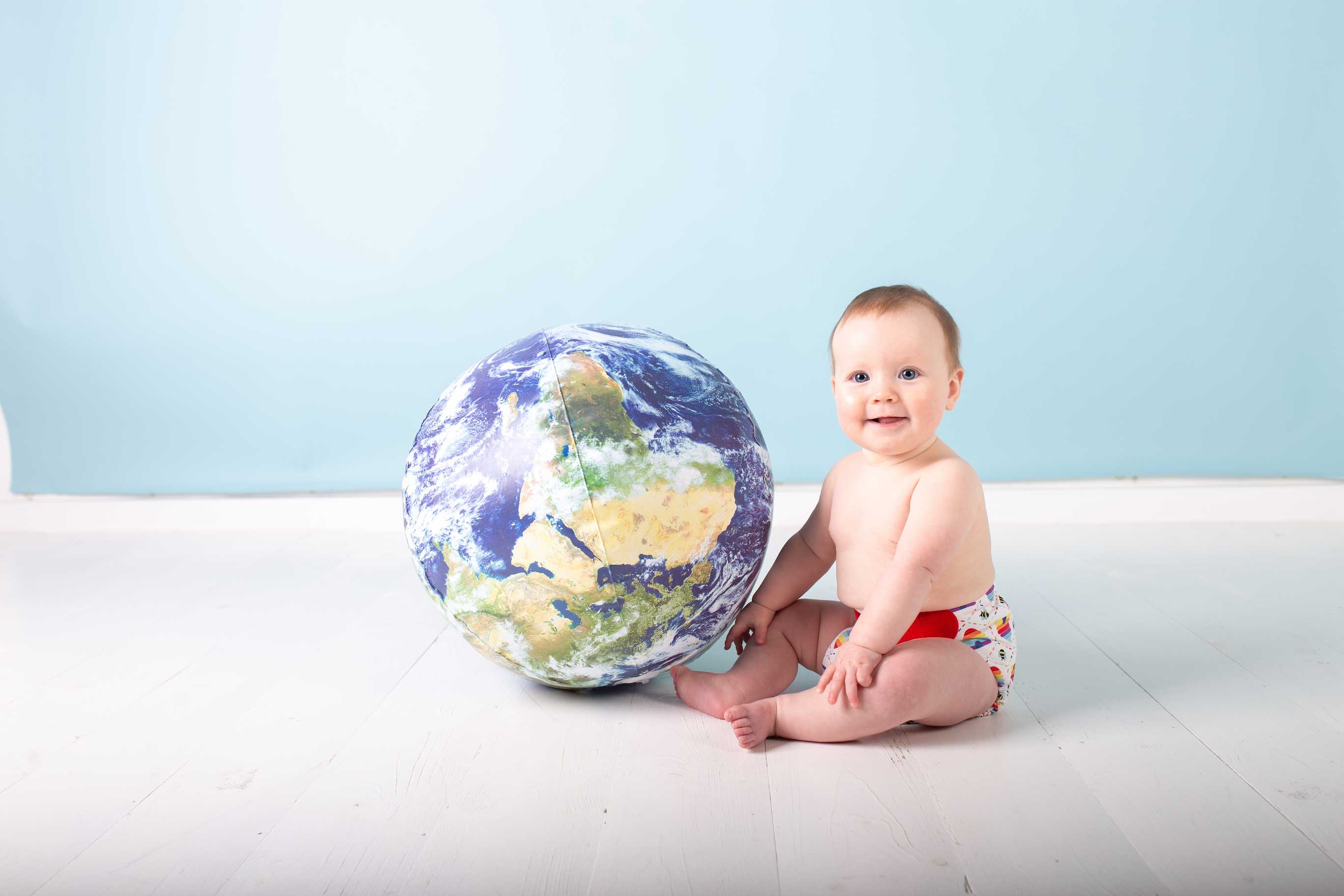 baby sat next to inflatable globe earth wearing TotsBots reusable nappies